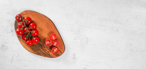 Poster - Vibrant small red tomatoes with green vines on wooden chopping board, white stone table under, view from above space for text right side