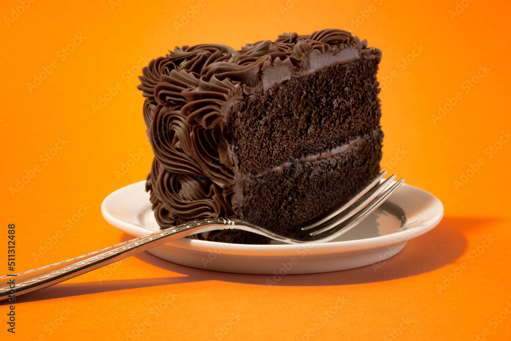 Slice of Chocolate Layer Cake on White Plate with Fork against Orange Background