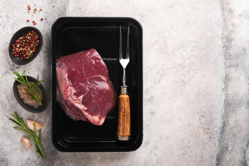 Wall Mural - Beef steak. Fresh raw beef steak with fork and rosemary in vacuum black plastic pack on grey stone background. Vacoom package. Top view. Mockup for design idea.