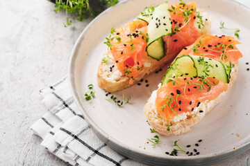 Sandwiches. Salmon toast with cream cheese, cucumber, black sesame and microgreens on gray concrete table background. Seafood. Healthy food. Top view.