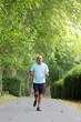 © NOWRA photography - Mature hairless man in sportswear jogging along a concrete path among the bushes and trees of nature