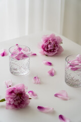 Sticker - fresh peonies and petals near glasses with gin tonic on white tabletop and grey background.