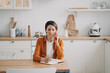© VK Studio - Young woman is call center assistant. Girl is sitting at table at kitchen and taking notes.