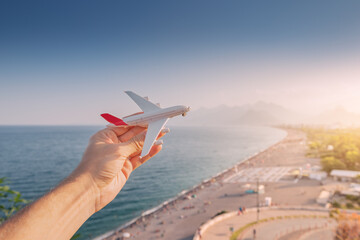 Toy airplane in hand against the background of the famous Konyaalti beach in Antalya - the main Turkish resort and riviera. Passenger traffic and flights to dream vacation