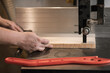 Close-up cropped hands of carpenter professional man hands using panel sizing saw woodworking machines. Pusher on table