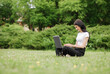 © Yuliia - Young woman sitting on green grass in a park with legs crossed on a summer day while using a laptop