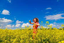 Young Pretty Woman In A Colored Dress On Lightning Cheerful Yellow Background Blooming Rapeseed Fields.