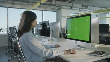 Asian Business Woman Working on Desktop Computer with Green Screen Mock Up Display in Busy Creative Office. Beautiful Diverse Female Manager Surfing Internet in Green Screen Notebook.