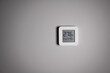 Electronic indoor white plastic digital thermometer on gray wall showing temperature, humidity level in house, smiling smiley face indoors in daylight sun