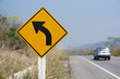 © Sanhanat - Yellow traffic sign with arrow left curve symbol beside the rural road to warn drivers to know the way ahead has a left curve. Concept : Warning traffic sign for transportation.