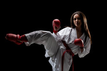 Girl Exercising Karate Leg Kick Wearing Kimono And Red Gloves Against Black Background..