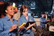 Two professional female engineer workers in safety uniforms work by inspecting machines' voltage current, checking, and maintaining at manufacturing factory, electric system service occupations.