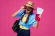 © khmelev - Winking woman traveler holds airplane ticket with passport. Explorer wearing denim t-short and sunglasses. Happy lady on isolated background. Studio shot