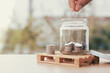 © THAWEERAT - Coins in a glass bottle, Hand of male or female putting coins in jar with money stack step growing growth saving money on nature background, Concept finance business investment.
