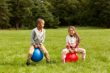 Wall Mural - childhood, leisure and people concept - happy children bouncing on hoppers or bouncy balls at park