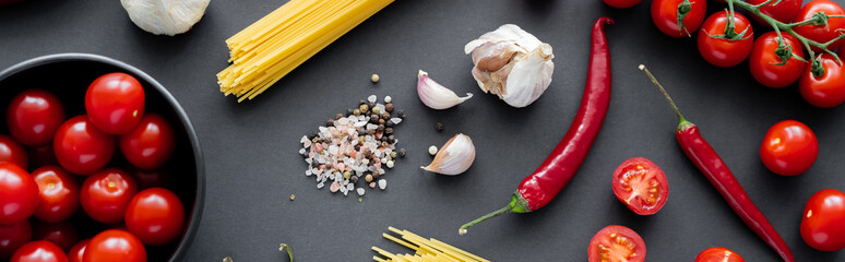 Canvas Print - Top view of fresh vegetables near spices with garlic and raw pasta on black surface, banner.