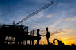 © เลิศลักษณ์ ทิพชัย - Silhouette of a male engineer standing at a construction site in the evening sunset. A team of construction engineers talks to managers and construction workers at an industrial construction project.