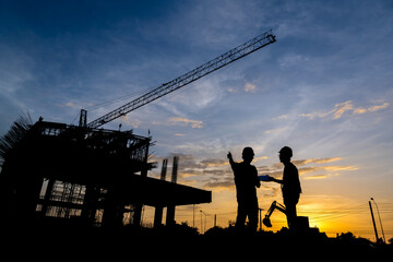 Silhouette of a male engineer standing at a construction site in the evening sunset. A team of construction engineers talks to managers and construction workers at an industrial construction project.