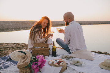 Wall Mural - Happy couple in love having romantic picnic, drinking wine on the beach at sunset.