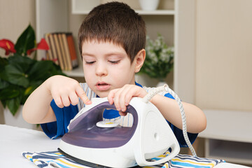 Wall Mural - A boy of 4 years learns to hold an iron, iron clothes on an ironing board. Helper, help children to care for the house.