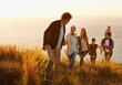© Mariusz S/peopleimages.com - Follow the leader. A multi-generational family walking up a grassy hill together at sunset with the ocean in the background.