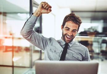 Its a victory worth celebrating. Shot of a handsome young businessman doing a fist pump while working on a laptop in an office.
