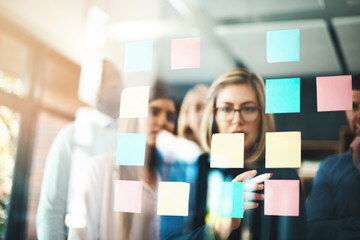 Wall Mural - Marketing ideas that match the company brand. Shot of a group of businesspeople arranging sticky notes on a glass wall in a modern office.