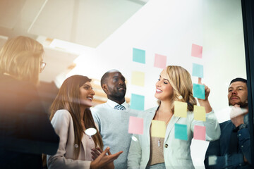 Poster - Marketers flexing their mental muscles. Shot of a group of businesspeople arranging sticky notes on a glass wall in a modern office.