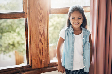 Wall Mural - Happy kids make happy homes. Portrait of a happy young girl standing next to a window at home.