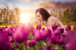 © edb3_16 - Caucasian Adult Woman smelling fresh Tulip Flowers in a field. Spring Season. Art Render. Sunset or Sunrise Sky