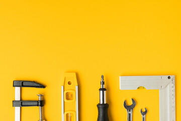 Handyman's tools. Flat lay of clamps, wrench, screwdriver, drill, angle, bubble level and tape measure on yellow background. Happy Father's Day. Free space  for you text