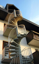 A Steep Spiral Staircase With Railings Leads Up The Outside Of The House.