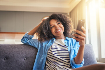 Poster - Time to see whats going on social media. Shot of a cheerful young woman browsing on her cellphone while being seated on a couch at home during the day.