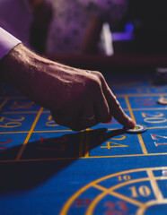 Wall Mural - Vibrant casino table with roulette in motion, with casino chips, tokens, the hand of croupier, dollar bill money and a group of gambling rich wealthy people playing bet in the background