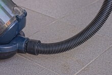 A Long Black Plastic Hose In A Blue Vacuum Cleaner Stands On A Gray Concrete Floor