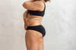 © Юля Бурмистрова - Cropped overweight fat woman pinching and checking volume of sides in black bikini. Excess skin problem after childbirth. Edema fibrosis skin. Loosing skin turgor. Emphasizing adiposity. Side view