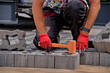 Majster ( foreman ) brukarz układa betonową  kostkę brukową . Brukowanie podjazdu ażurowymi bloczkami betonowymi z malutkimi dziurkami . Mistrzowsko wybrukowany podjazd . W użyciu pomarańczowy młotek.