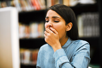 Poster - The student life isnt all that easy to keep up with. Shot of a university student yawning while working on a computer in the library at campus.