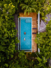 Wall Mural - couple of men and women in a swimming pool in the jungle of Krabi Thailand, aerial view with a drone above swimming pool in the jungle of Thailand. 