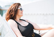 © Galina Zhigalova - Stylish happy young woman plus size body positive in black swimsuit and sunglasses enjoing life rest on beach lounger near the pool, summer vacations
