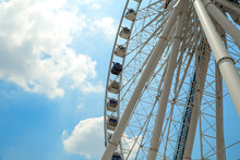 Giant Ferris Wheel With Numbered Cabins In The Park - Bright Blue Sky With Sharp Clouds Behind It.