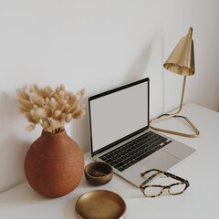 Wall Mural - Aesthetic minimalist home office workspace desk. Laptop computer with blank copy space display screen, glasses, dried grass bouquet, lamp, golden plate. Chic lady boss business branding concept
