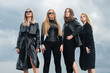 Group of elegant people. Fashion portrait of group fashion models girls posing outdoor, black style outfit against sky. Attractive young vogue women. Stylish casual clothes.