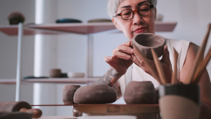 Asian elderly woman enjoying pottery work at home. A female ceramicist is making new pottery in a studio.