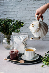 A teapot in a hand pours tea into a white cup a drop of tea with jam and honey flies white background greens