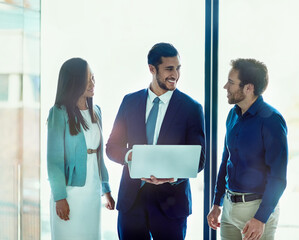 Poster - Finding corporate solutions together. Shot of three businesspeople working together on a laptop while standing in an office.