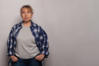 © millaf - Middle age senior woman in grey t-shirt standing against grey studio wall background