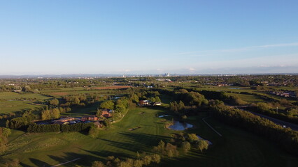 Poster - Aerial view looking down onto a golf course surrounded by green fields with the Manchester skyline in the distance. 