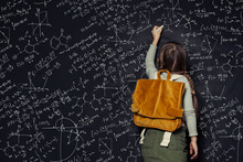 Child Girl Against Big Blackboard With Formulas, Back View
