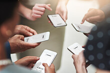 Staying Simultaneously And Instantly Connected Together. Cropped Shot Of A Group Of Unrecognisable Businesspeople Texting On Their Cellphones In An Office.